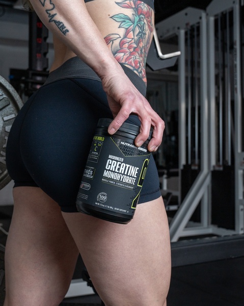 A close-up, high-contrast shot featuring an athlete holding a creatine supplement container against a gym background.